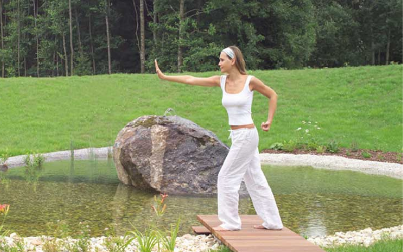 Eine Frau macht an einem Teich Qi Gong
